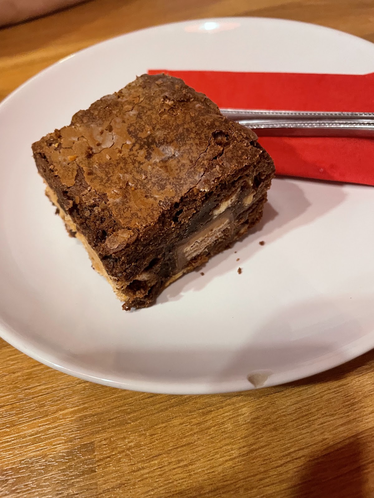 A thick fudgy brownie studded with chunks of chocolate bar on a shortbread base, on a white plate.